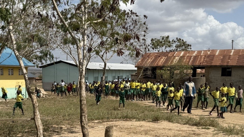 A small Kenyan community gathered at dusk outside a church and school, in conversation
